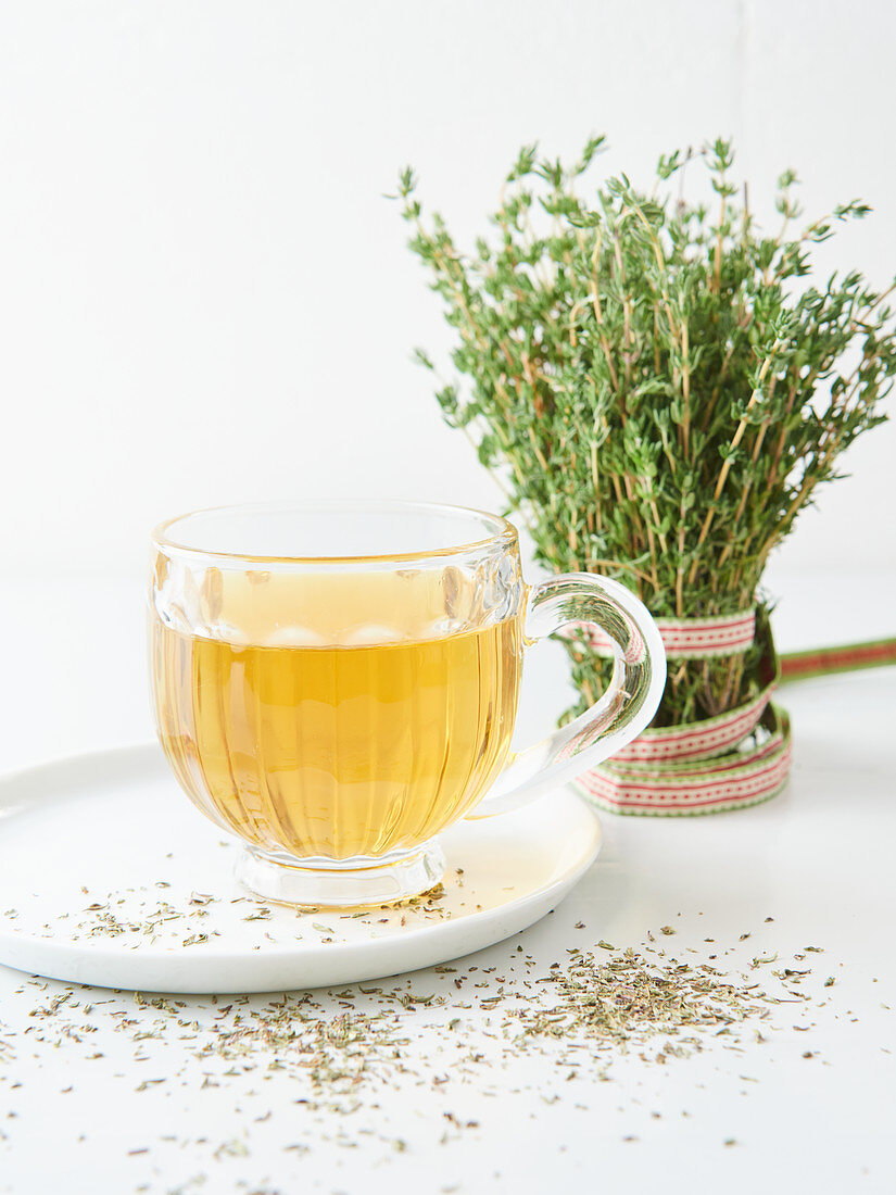 Thyme tea in a glass cup in front of a fresh bunch of thyme