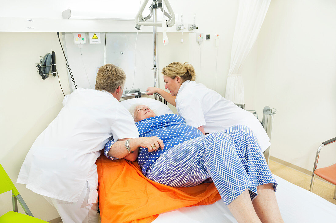 Nurses preparing to move a patient using a sling hoist