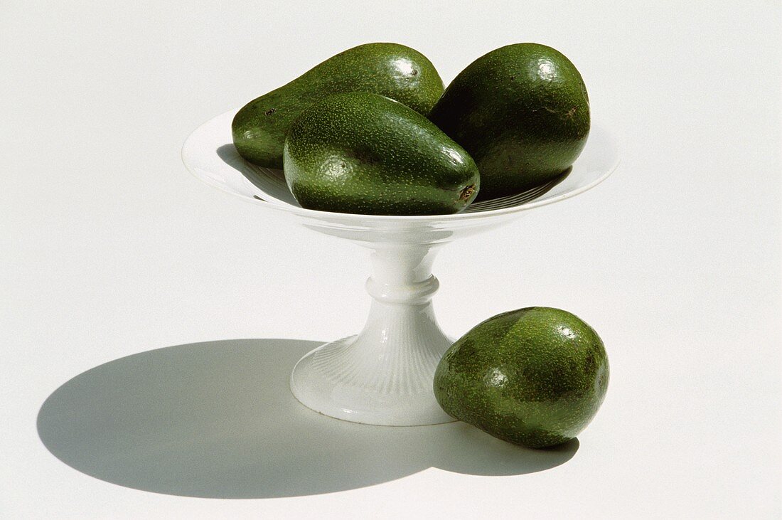 Three avocados in tall bowl and one beside it
