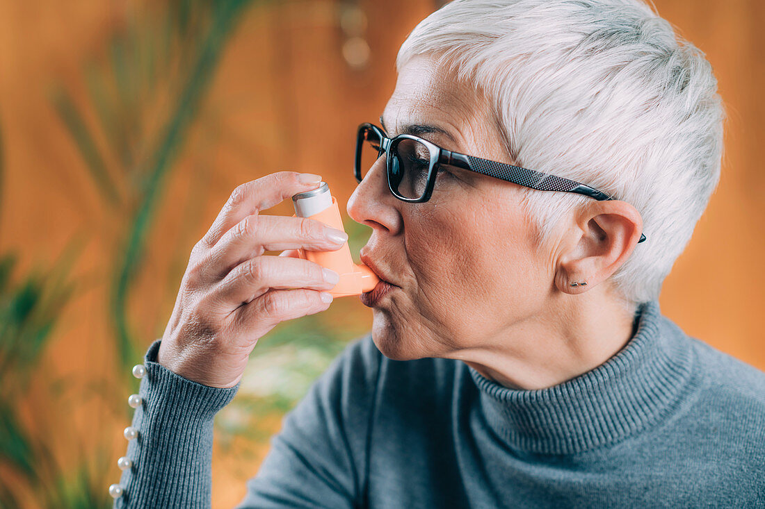 Senior woman using asthma inhaler with extension tube