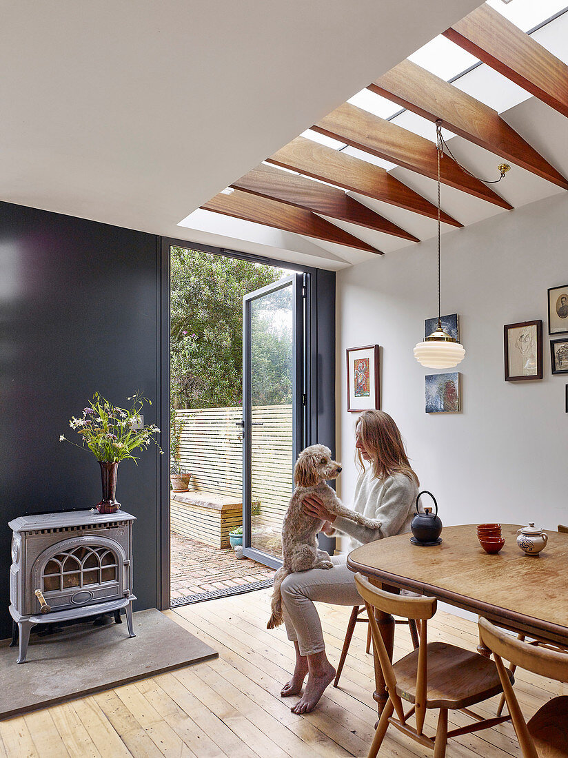 Woman and dog at dining table below skylight and next to door leading into garden