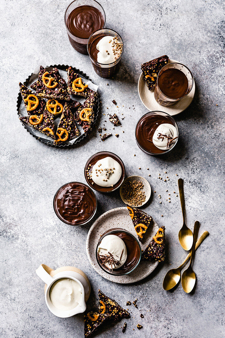 Individual chocolate puddings served with whipped coconut cream and a pretzel bark.
