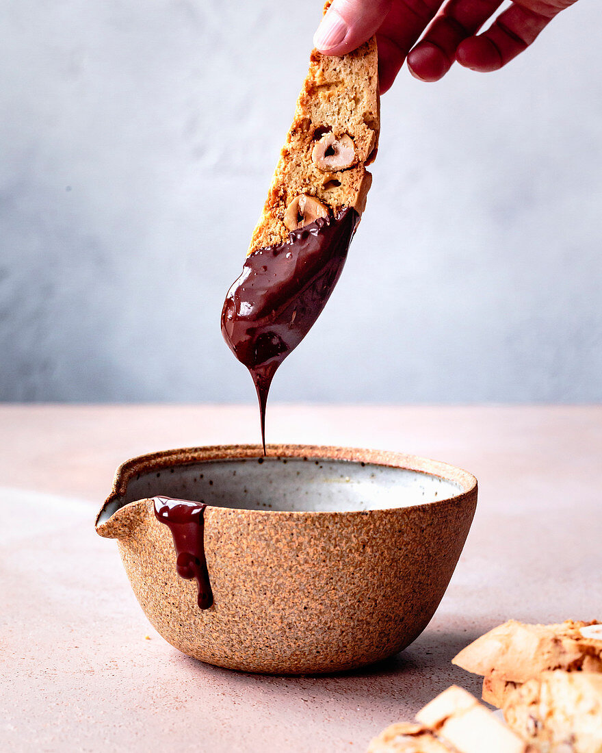 Hand taucht Haselnuss-Biscotti in geschmolzene Schokolade