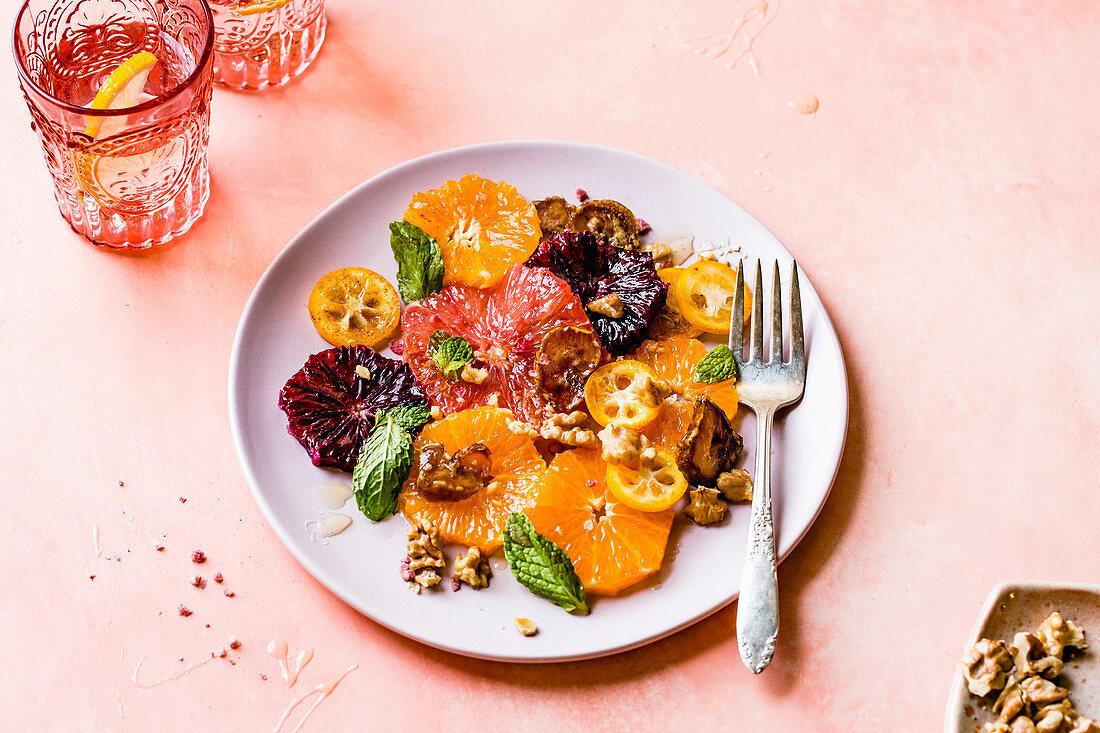 Citrus fruit salad served on a plate beside glasses of lemon water.