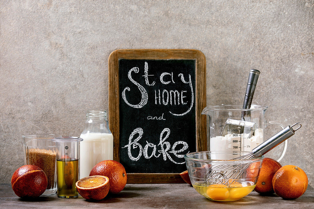 Kreidetafel mit Aufschrift 'Stay home and bake' zwischen Backzutaten