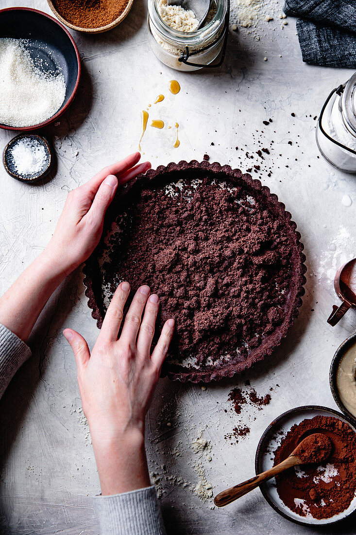 Hands preparing a chocolate tart crust.