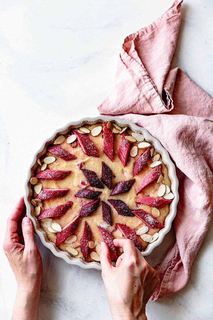 Pieces of rhubarb placed on cake batter by a hand.