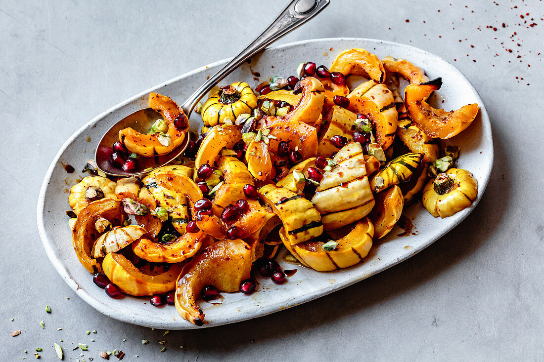 Roasted delicata squash with pomegranate and pistachios on a plate.