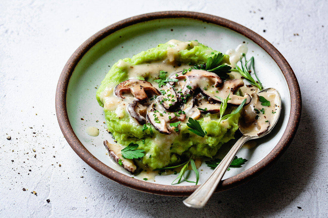 Closeup view of green mashed potatoes with mushroom gravy on a plate.