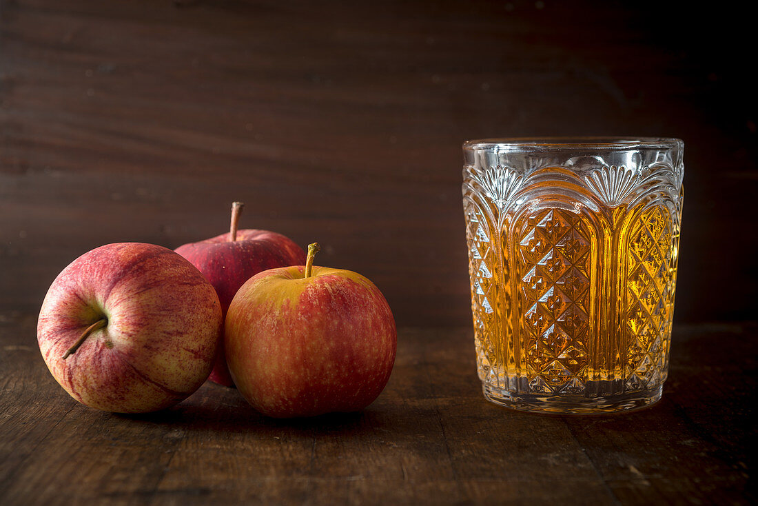 Drei Äpfel und ein Glas mit Apfelsaft auf Holzuntergrund
