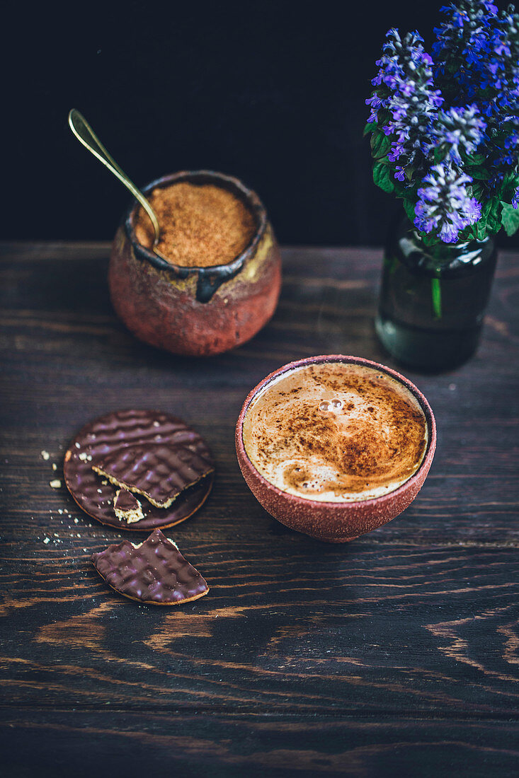 Kaffee in Keramikbecher daneben Schokoladenplätzchen auf rustikalem Holztisch