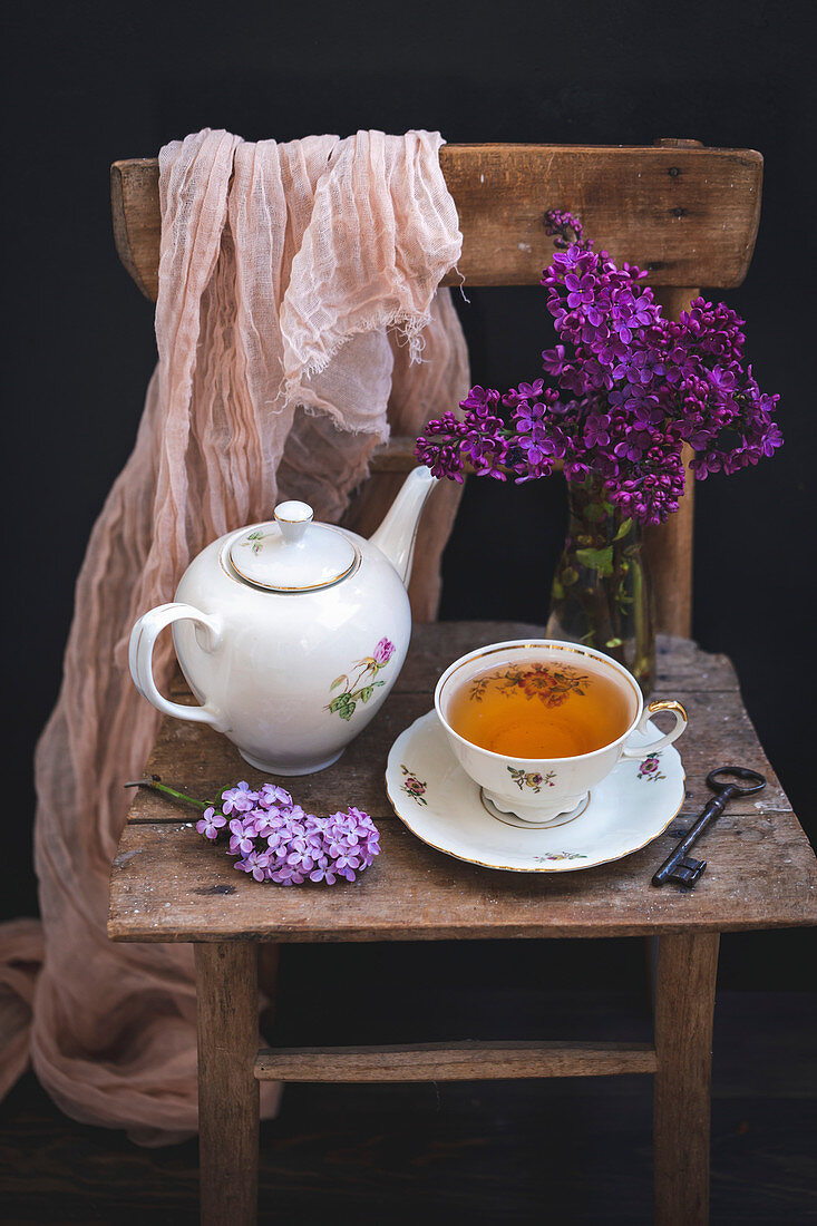 Teekanne und Tasse Tee serviert auf rustikalem Holzstuhl