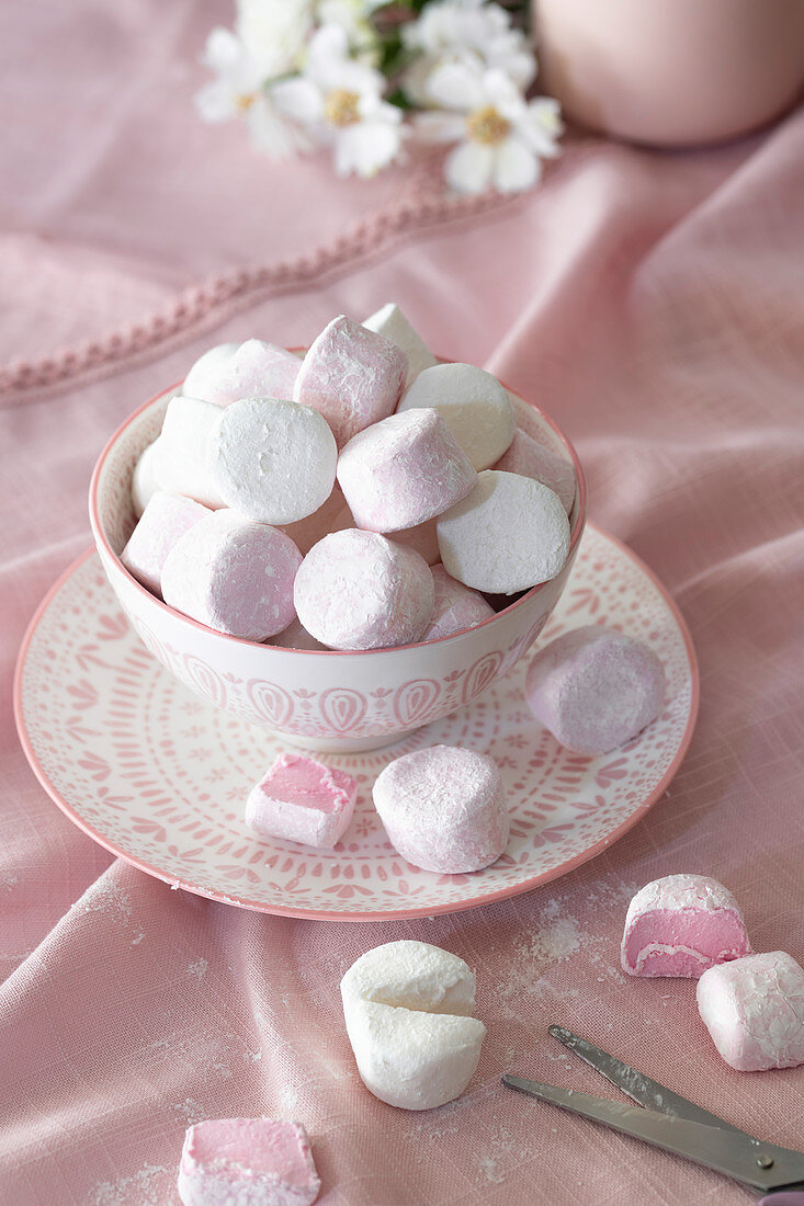 Round pink and white marshmallows in a bowl with two cut in half with scissors.
