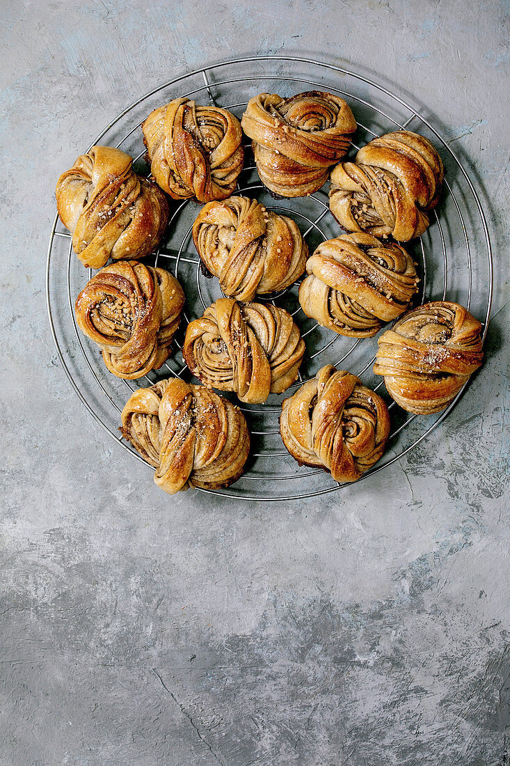 Traditional Swedish cardamom sweet buns Kanelbulle on cooling rack over grey concrete texture background. Flat lay, space