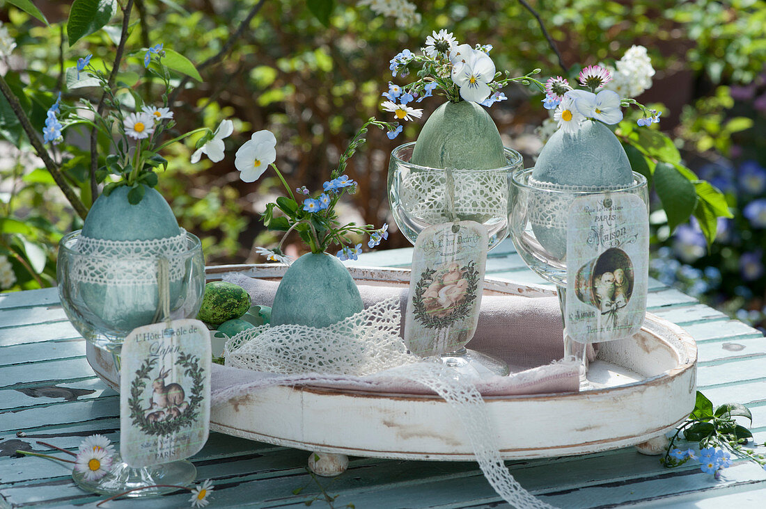 Small bouquets of horned violets, daisies and forget-me-nots, Easter eggs with lace ribbon as vases, nostalgic pendants