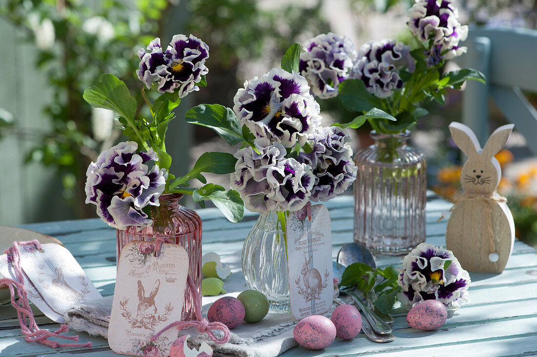 Vasen mit gekräuselten Stiefmütterchen 'Purple White Rim' als Osterdeko mit Ostereiern, Osterhase und Anhängern