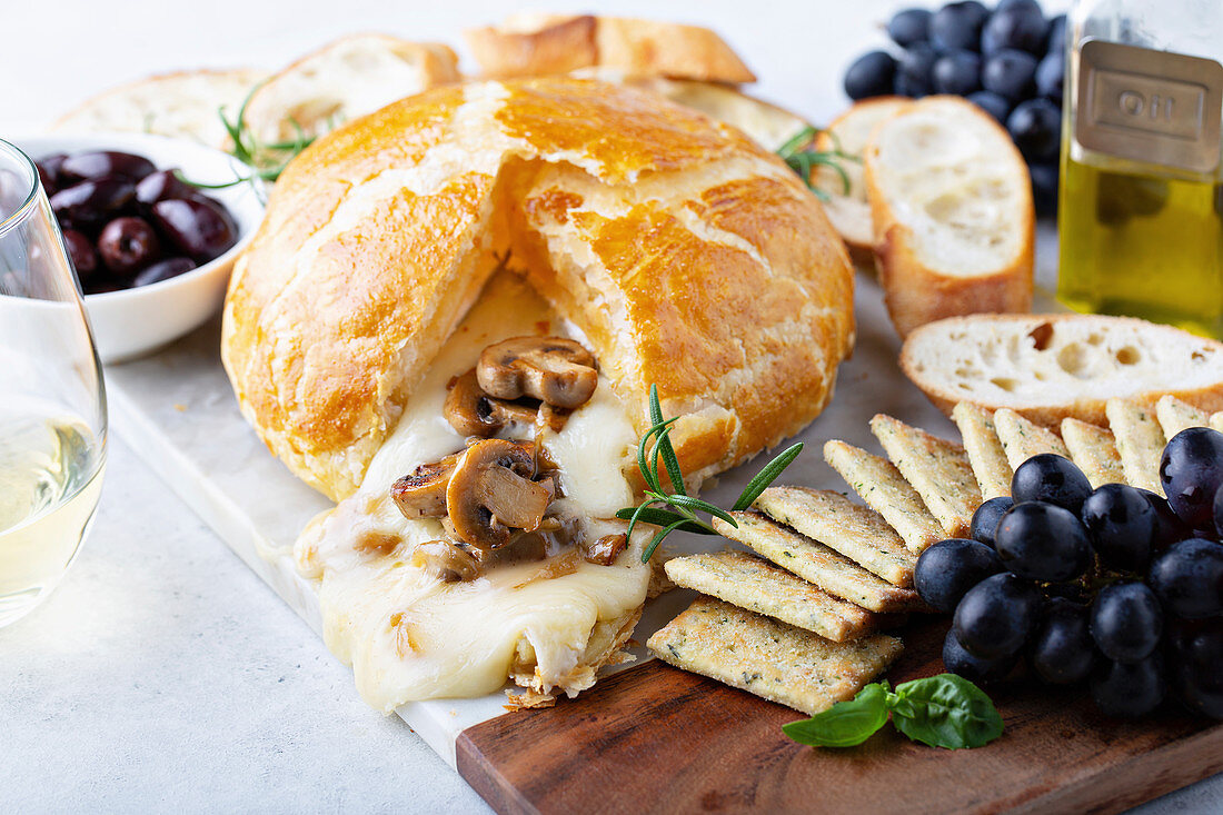 Gebackener Brie im Blätterteig mit Pilzen, Brot und Crackern auf Brett