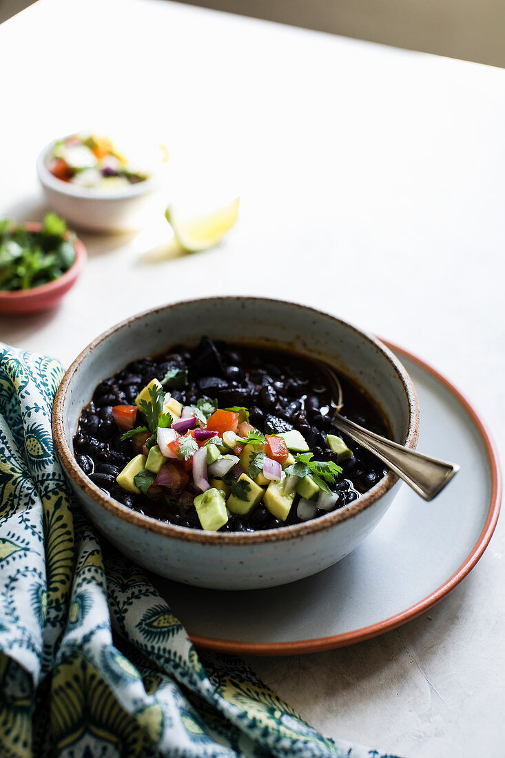 Black beans with avocado, tomato, red onion and cilantro in a ceramic bowl.