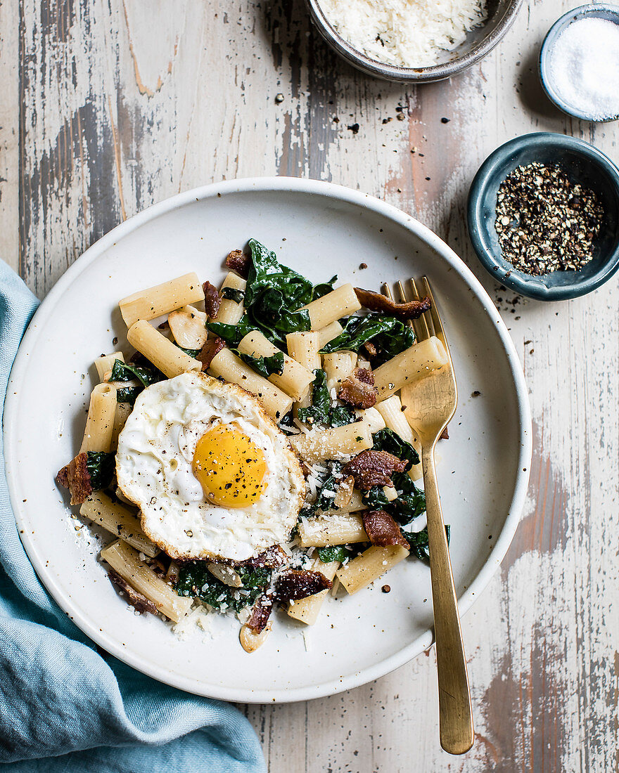 Penne pasta with spinach, bacon and a fried egg on a plate.