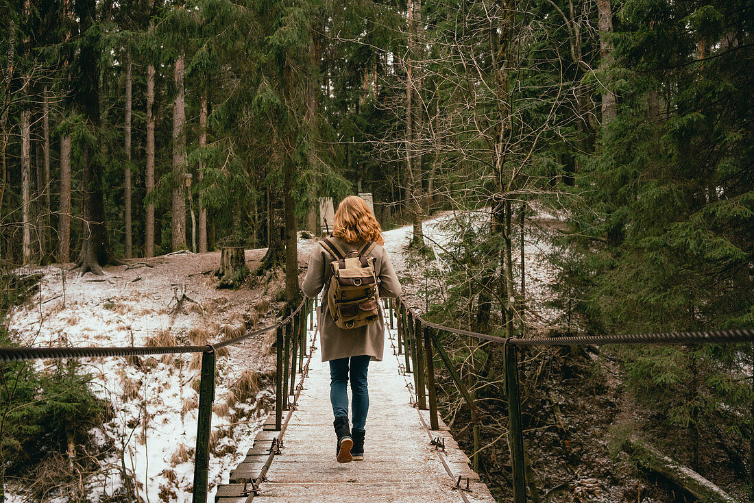 Rothaarige Frau mit Rucksack auf Fußgängerbrücke in verschneitem Wald