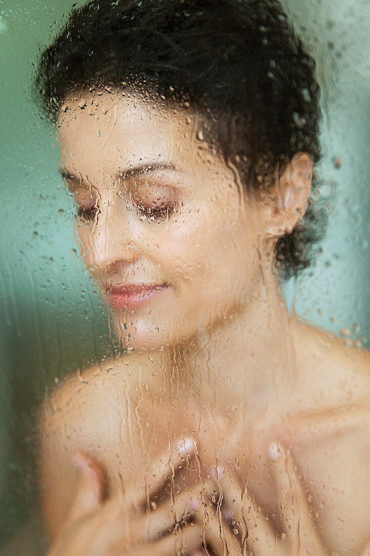 Sinnliche Frau beim Duschen hinter nassem Glas