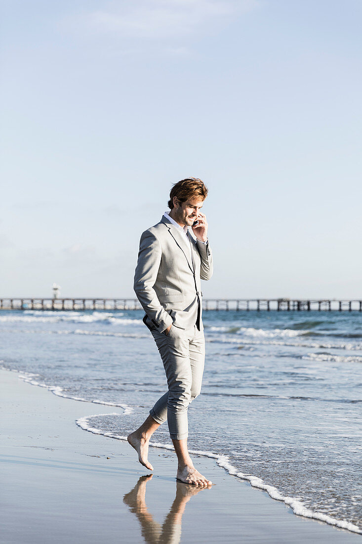 Geschäftsmann barfuß telefoniert mit einem Smartphone am sonnigen Strand am Ozean, Los Angeles, Kalifornien
