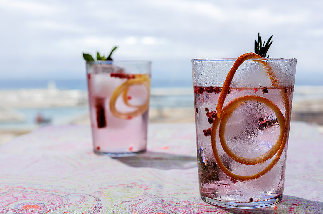 Rosa Gin Tonic mit rosa Pfeffer, Minze, Zimt und Orange im Sonnenlicht auf Restauranttisch