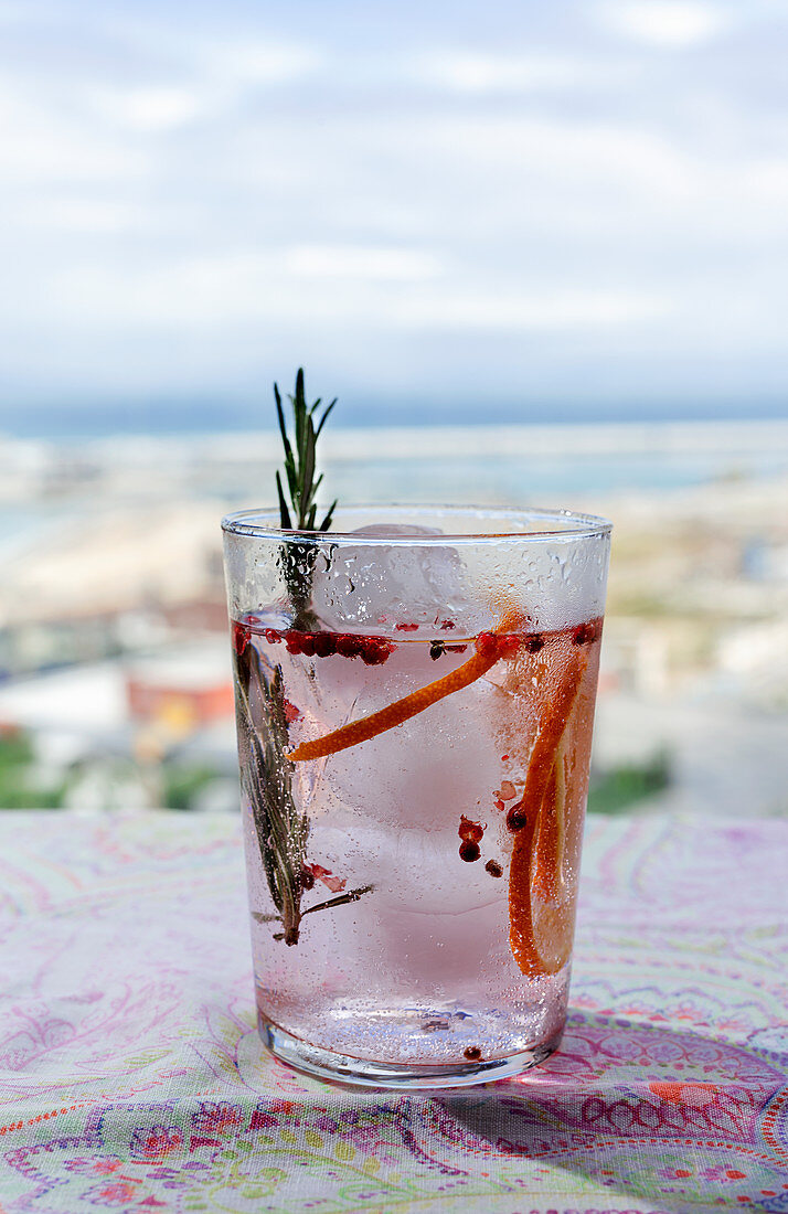 Rosa Gin Tonic mit rosa Pfeffer, Rosmarin und Orange im Sonnenlicht auf Restauranttisch