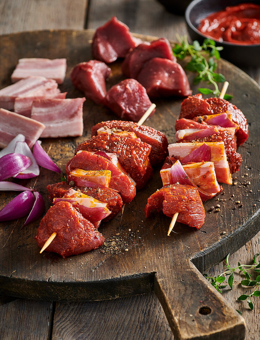 Rohe Wildfleisch-Spieße mit Speck und roten Zwiebeln auf Holzbrett