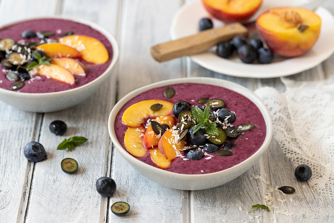 Blueberry smoothie bowl with peach slices, blueberries and pumpkin seeds