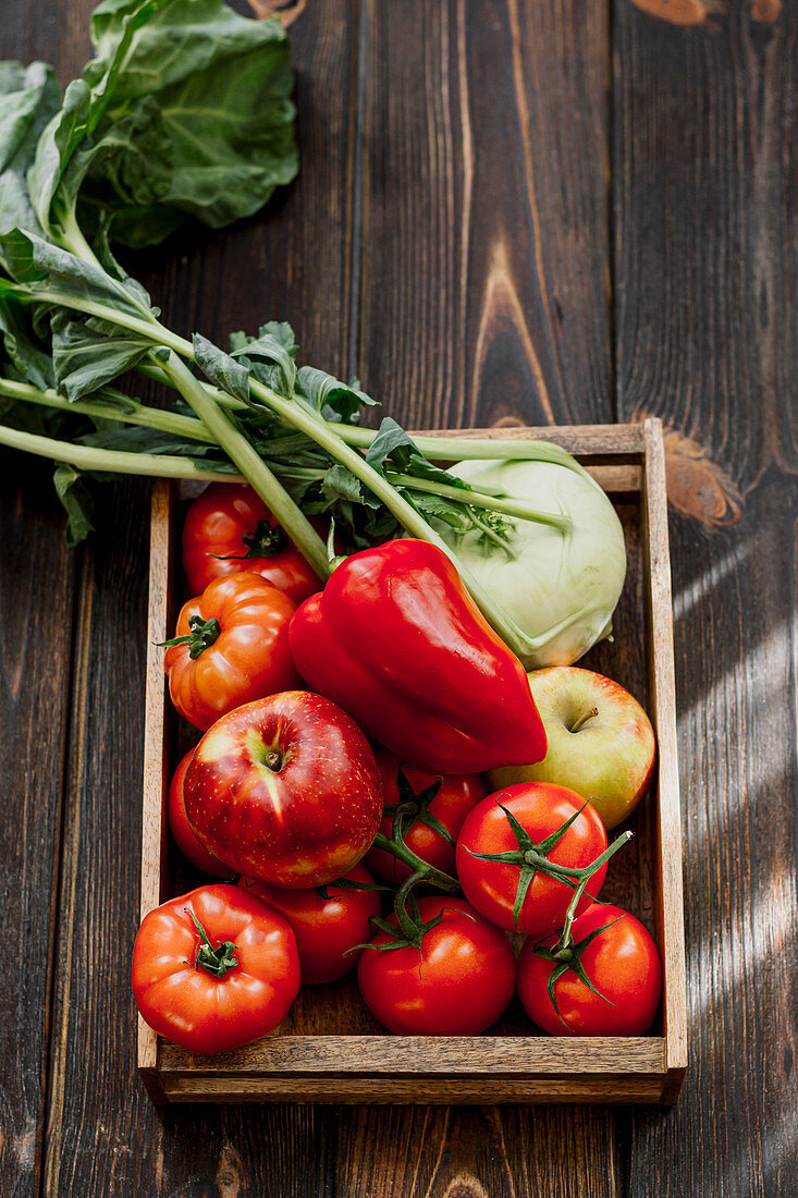 Apfel, Kohlrabi, Tomaten und rote Paprikaschote in Holzkiste