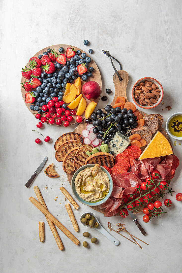 Feinkostplatte mit Schinken, Käse, Hummus, Oliven, frischem Obst und Brot