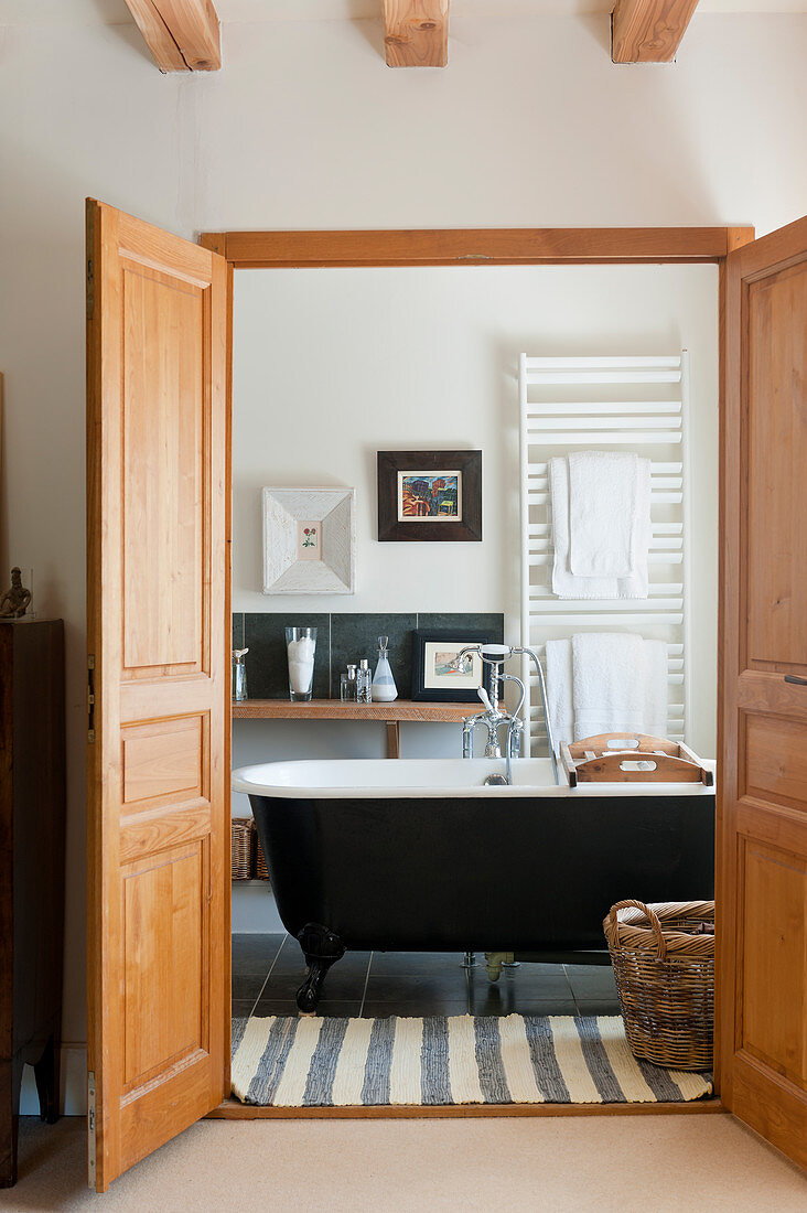 View through open double doors into bathroom with freestanding bathtub and striped rug