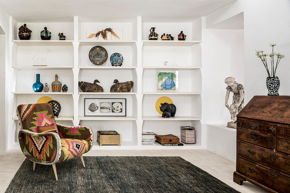 Upholstered armchair and shelves of African art in farmhouse