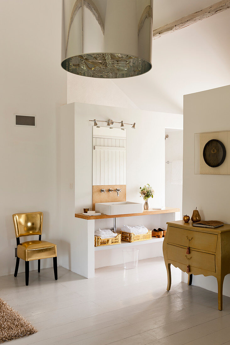Glamourous gold chair in white open plan bathroom with French drawers