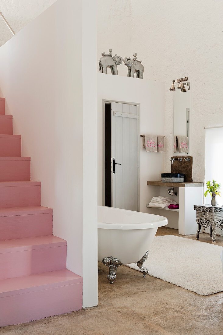 Pink staircase in open plan bedroom with freestanding bath