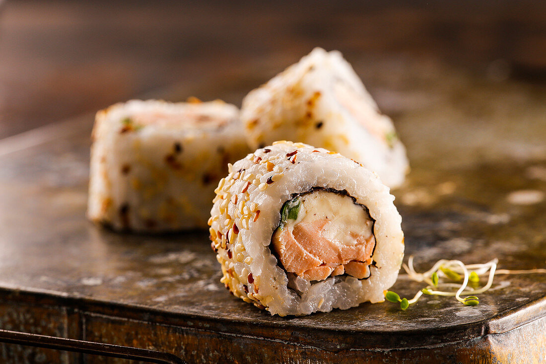 Sushi roll with salmon, cream cheese and green onion covered with sesame seeds
