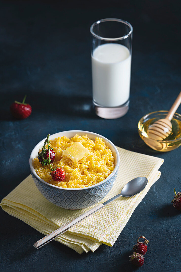 Corn porridge with butter and strawberries in a bowl with milk and honey