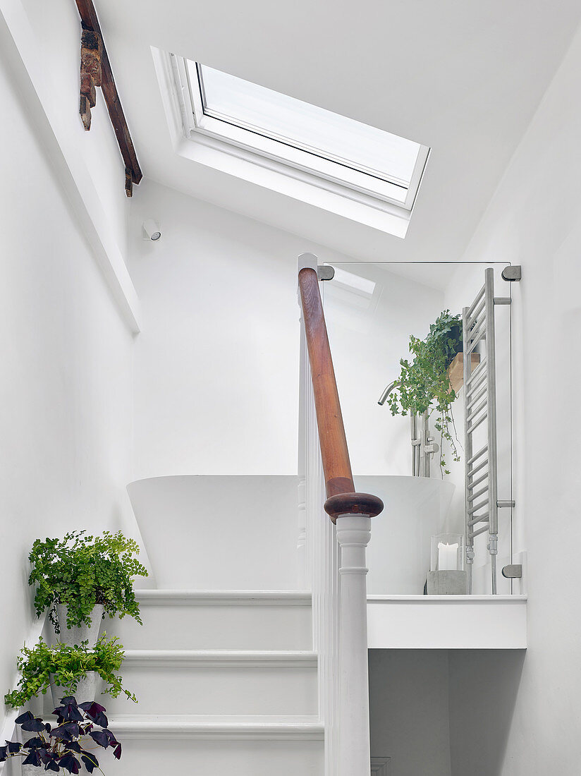 Steps leading to white, free-standing bathtub on landing below sloping ceiling