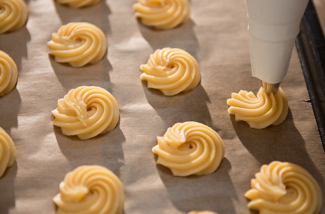 Choux pastry rosettes being piped onto baking paper