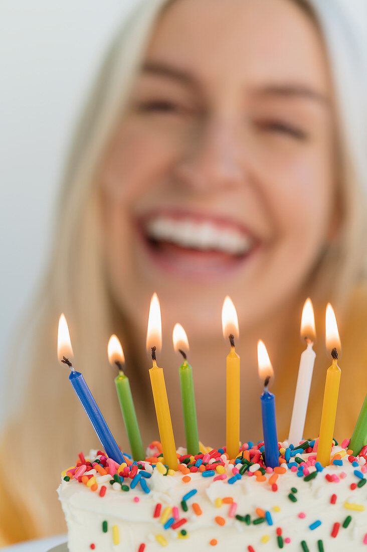 Lächelnde Frau vor Geburtstagstorte mit brennenden Kerzen
