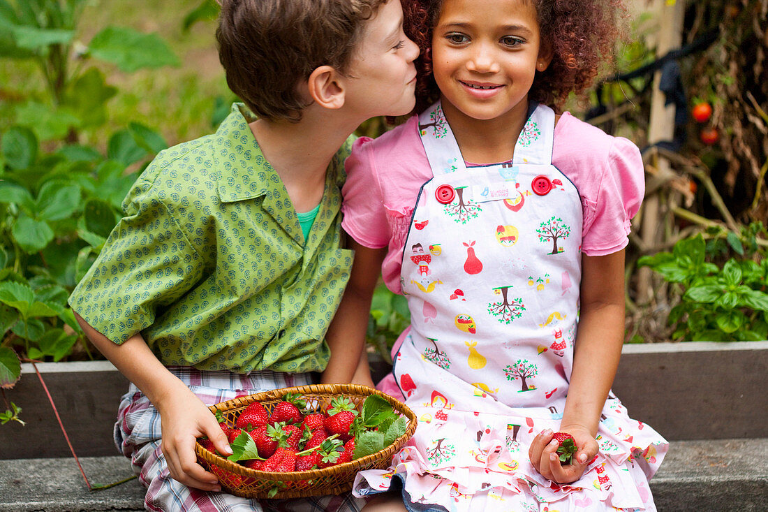 Zwei Kinder mit einem Korb Erdbeeren im Garten