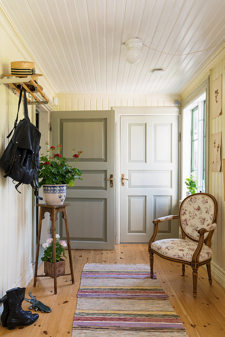 Plant stand and armchair in hallway with white-painted, wood-clad walls