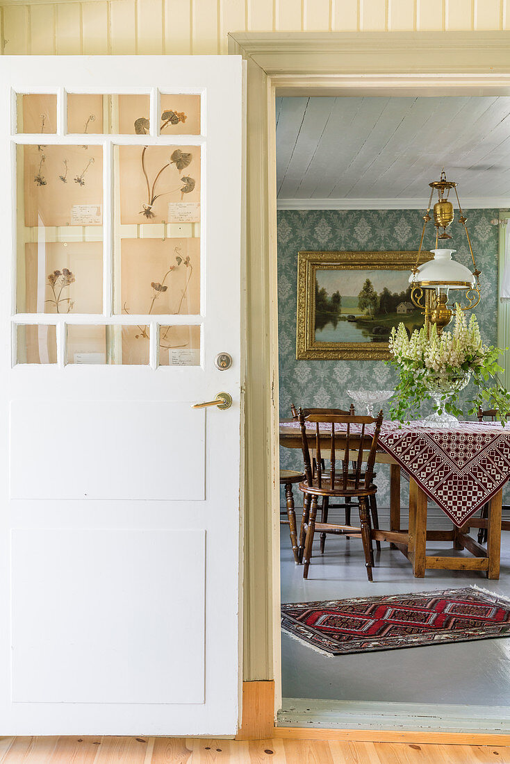 View into dining room with wooden table and painting on wall with patterned wallpaper