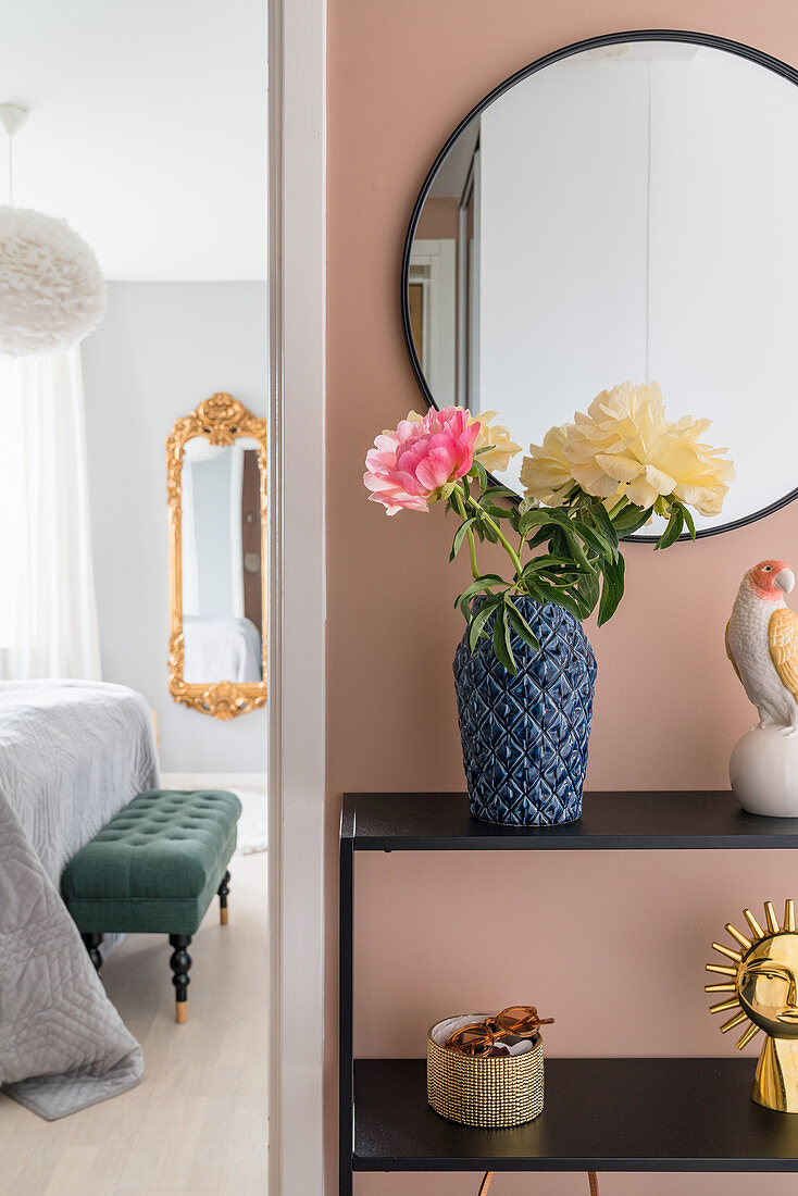 Sideboard below mirror on peach-coloured wall of hallway with view into bedroom