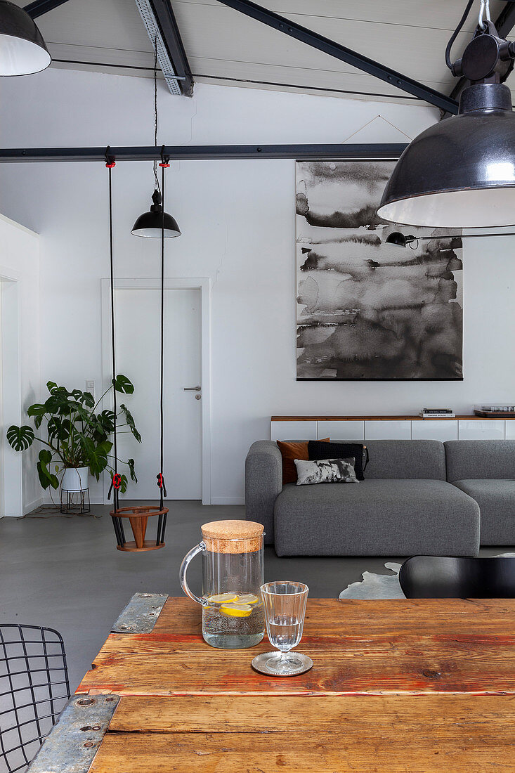 View over rustic dining table to grey sofa and child's swing in loft apartment