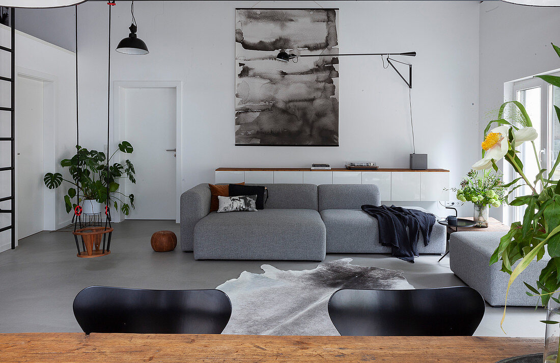 View over rustic dining table to grey sofa and child's swing in loft apartment