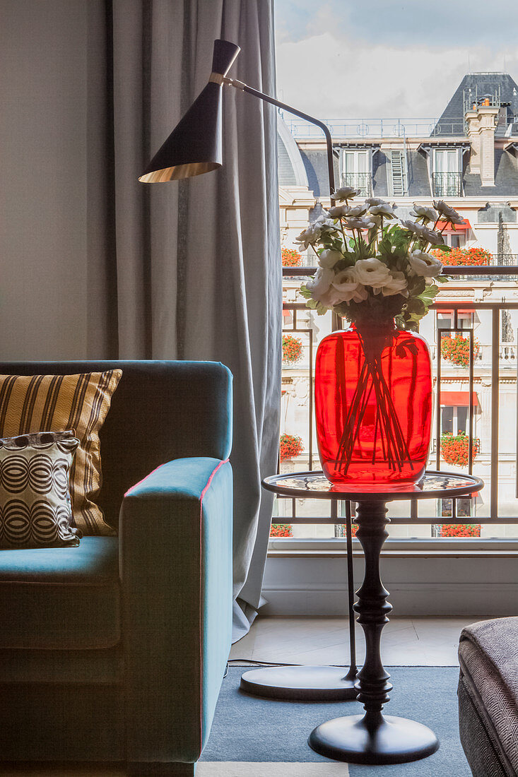 Red glass vase on side table and standard lamp next to French windows