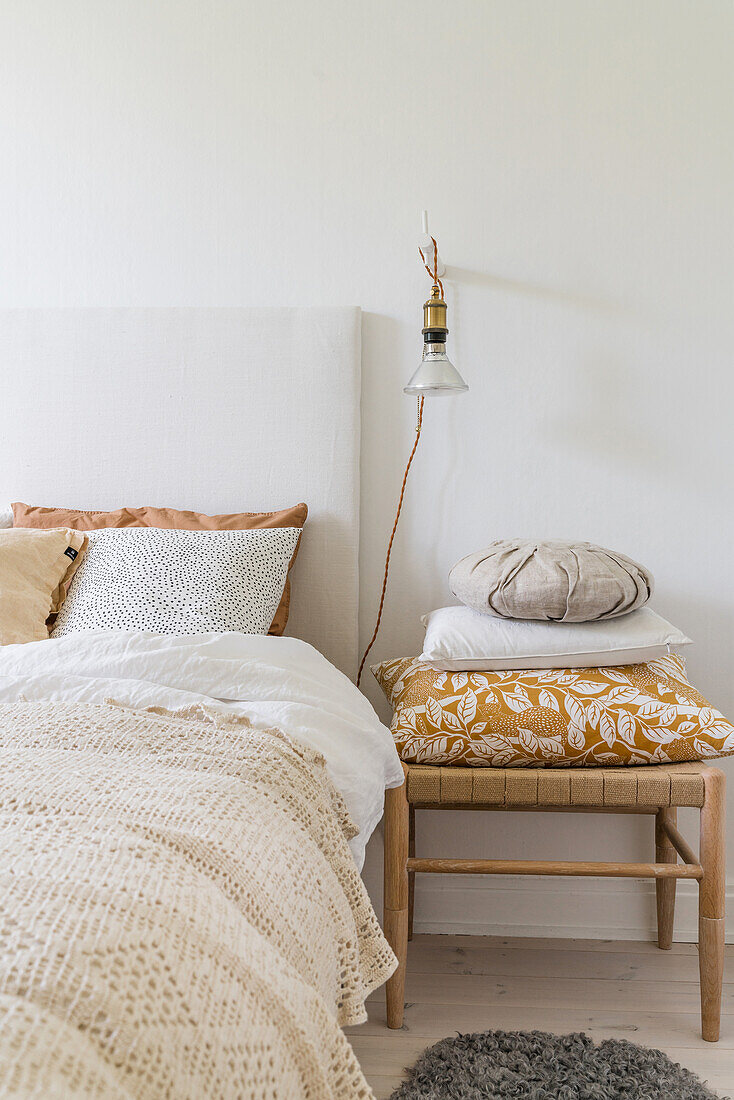 Doppelbett mit gehäkelter Tagesdecke, Wandleuchte und Hocker mit Kissen