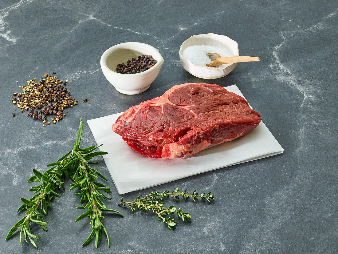 Raw sirloin steak on a piece of paper surrounded by herbs and spices